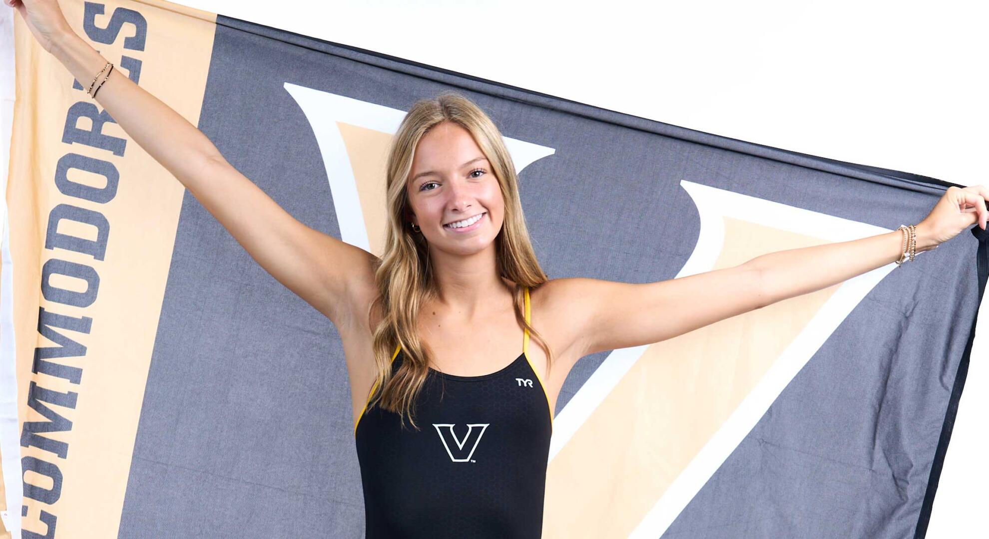 Swimmer Aubrey Hull smiles while holding a Vanderbilt Commodores flag up behind her.
