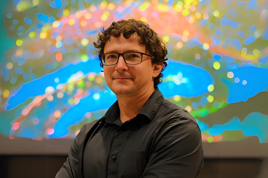 Headshot of Rick Sando standing in front of a colorful abstract background. 