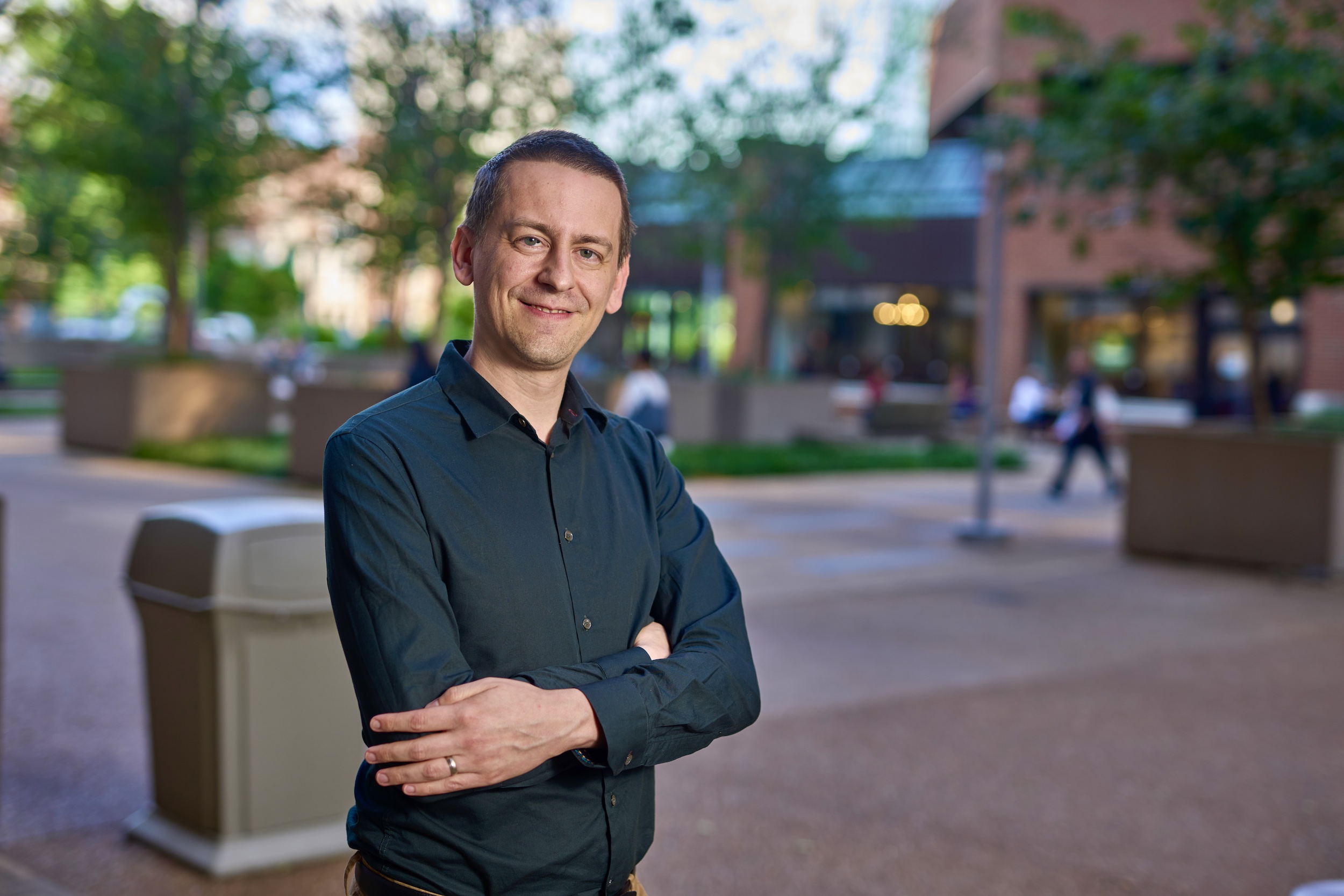 John Jumper stands outside in a black button-down with his arms crossed. 