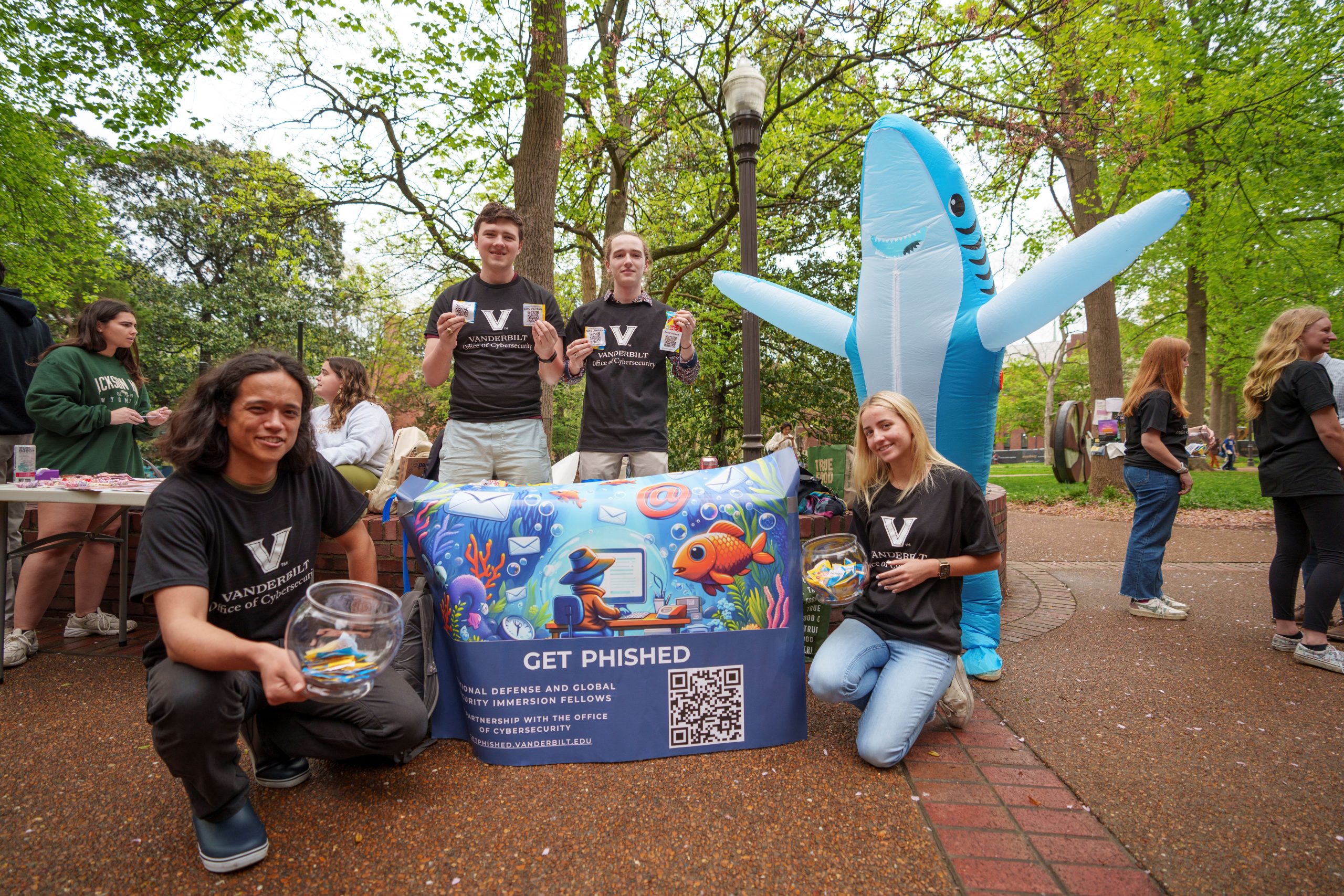 Students, including one dressed in a shark costume, pose for a photo with a sign that says "Get Phished" for their Immersion Vanderbilt project.  