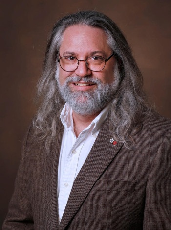 studio headshot of Phillip Franck in white collared shirt with brown jacket