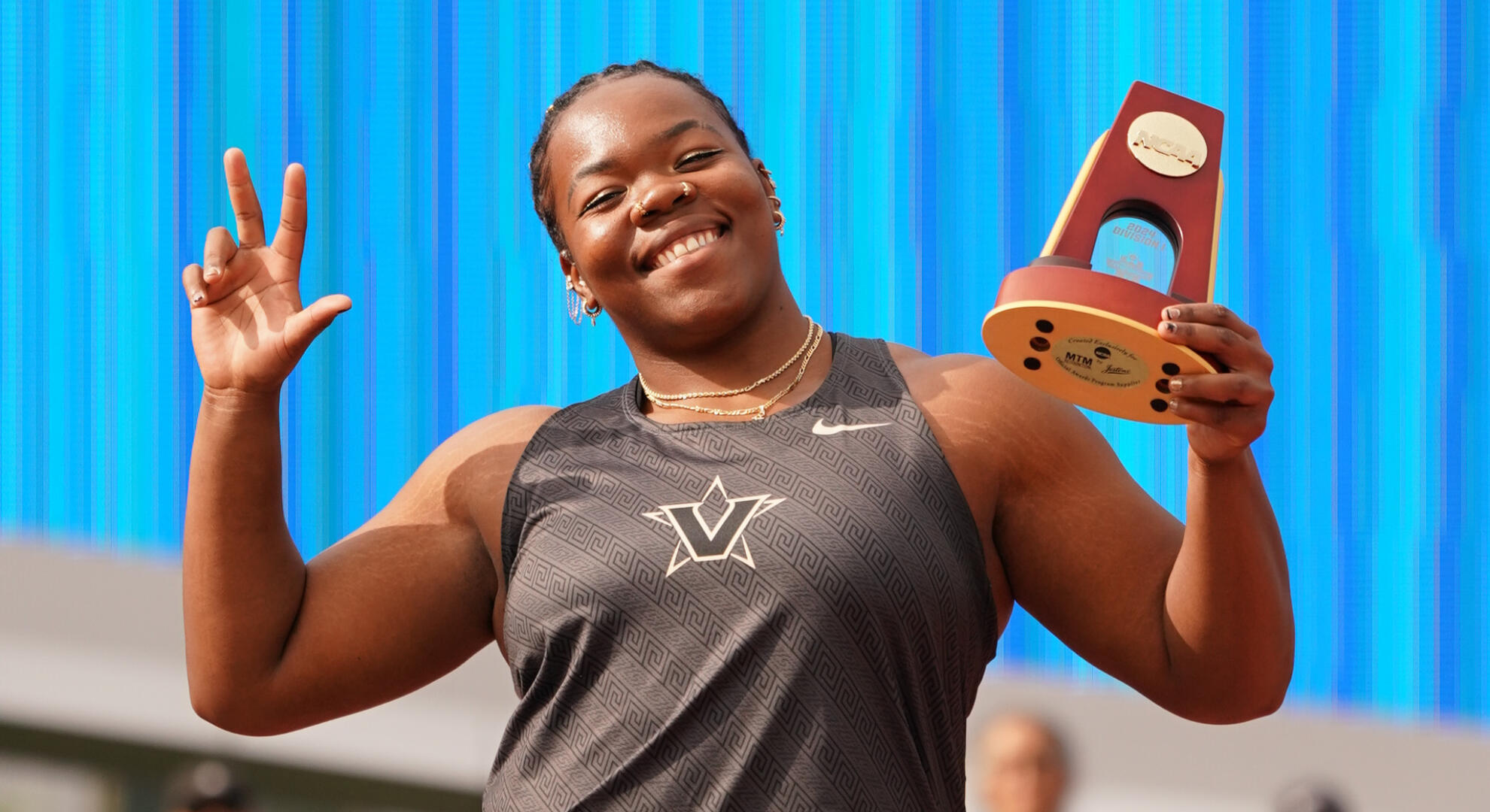 Veronica Fraley throws the Vanderbilt "V" hand sign while posing with her NCAA discus championship trophy.