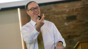 Pictured: Professor Josh White engages with his students at Vanderbilt Business to teach complex finance topics. He uses instances like the Reddit IPO case to enhance learning. In this photo, he is standing at the front of a classroom, smiling and pointing to a student. The student is not in the frame of the picture, but they are raising their hand to speak.