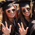 Two students give the Vanderbilt "V" hand sign while smiling in their commencement regalia