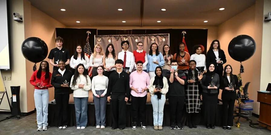 Students pose for a group picture on a stage with balloons