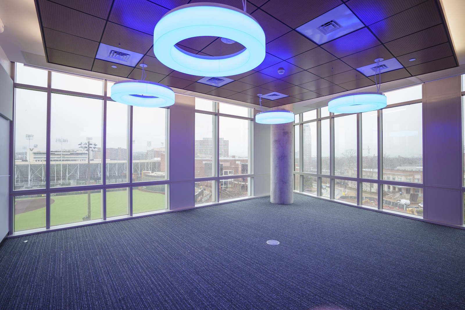 An empty room that will be used as a research space overlooks Hawkins Field. The ceiling features donut-shaped lights that glow a neon blue. 