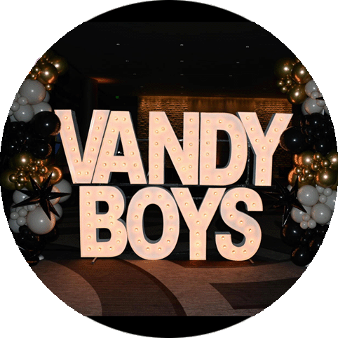  Large, illuminated marquee letters spelling ''VANDY BOYS''. Surrounding the letters are clusters of black, white, and gold balloons.