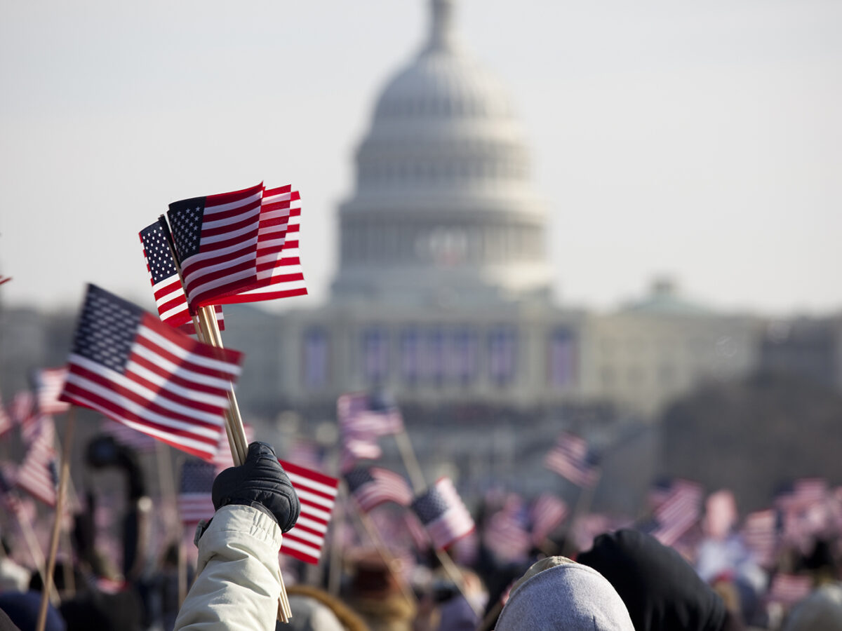 Stock image of people waving small American flags in front of the U.S. Capitol building