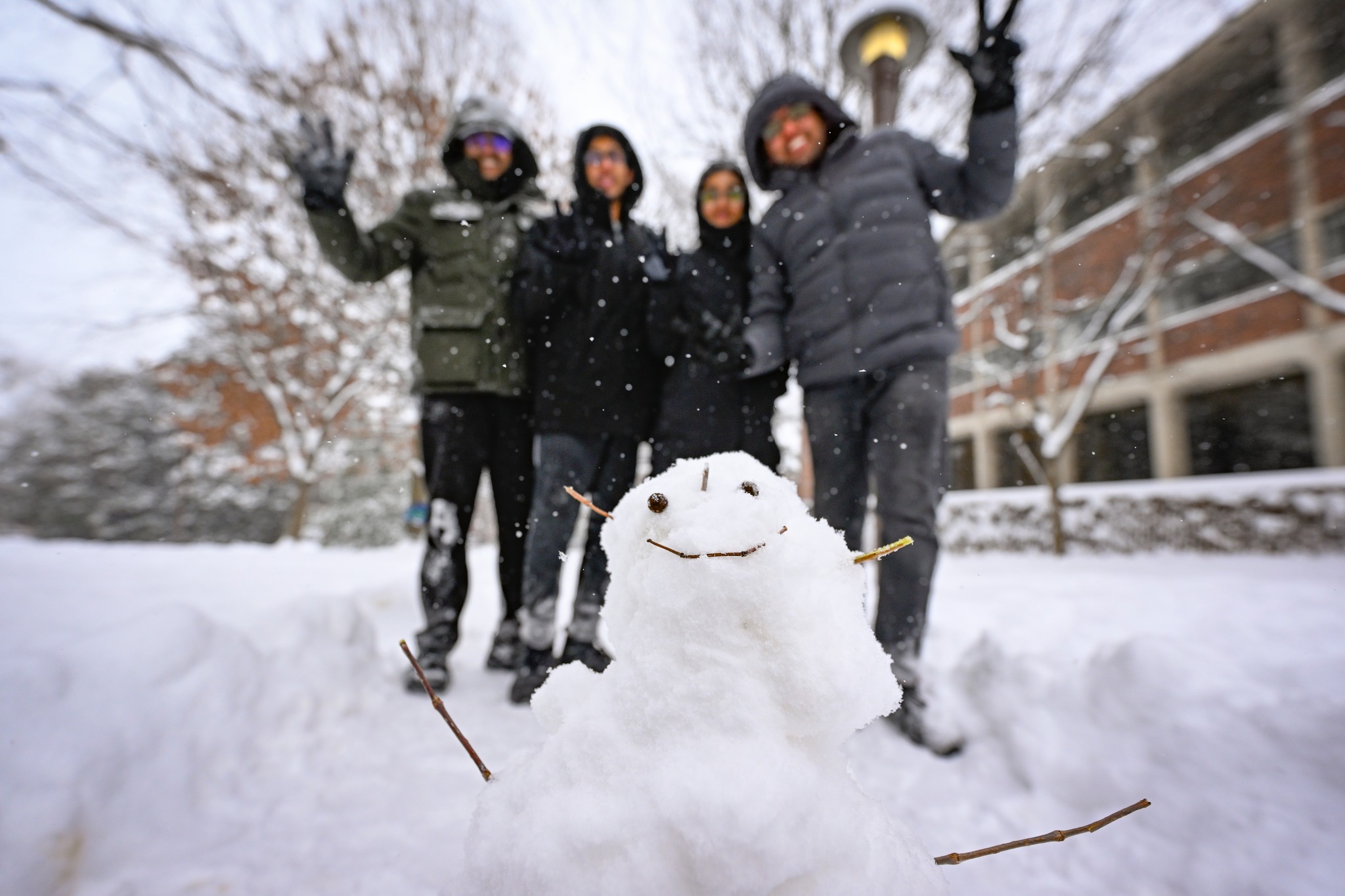Four students throw up the VU hand sign behind a snowman they made during the January 16 snow day. 