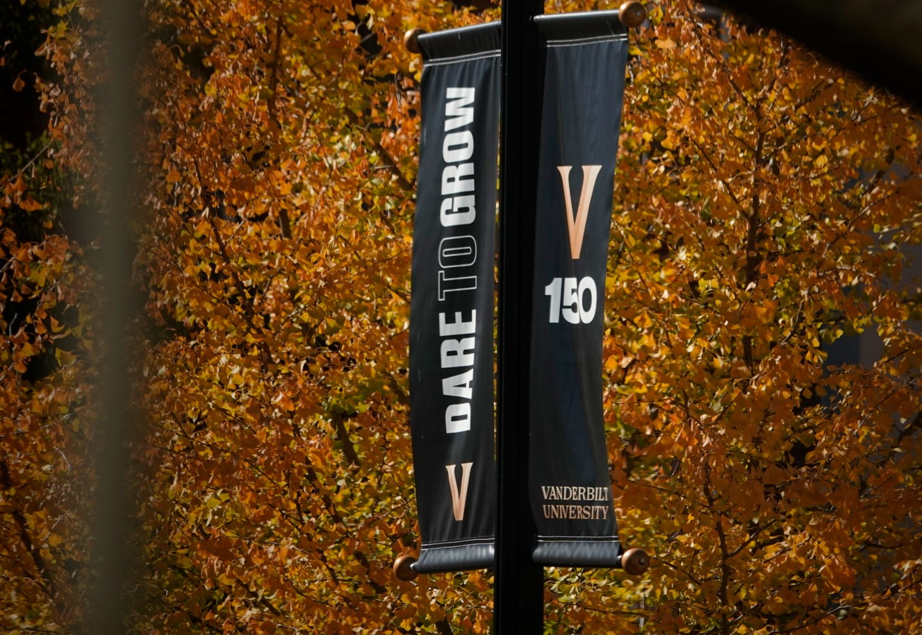 A "Dare to Grow" and "V150" banner hangs on campus surrounded by the leaves of autumn trees. 