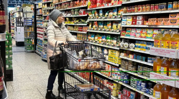 Pictured: A woman is pushing a shopping card down an aisle in a grocery store.