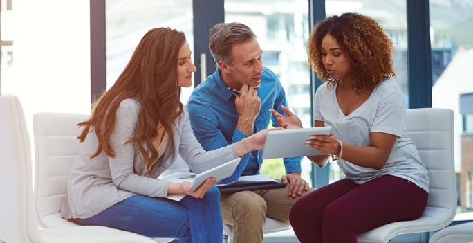 A white woman and white man listen to an African American woman explain her ideas in a work meeting