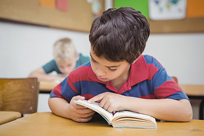 boy at table reading a book, using his finger