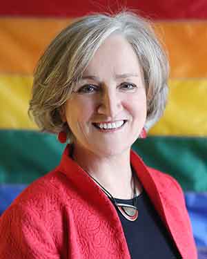Professor Tonda Hughes stands in front of a rainbow flag