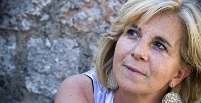 A smiling woman in her 50s in front of a rock wall.