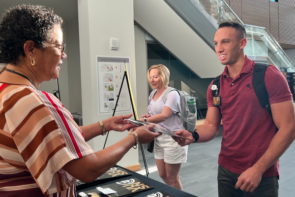 smiling person hands a smiling student a folder