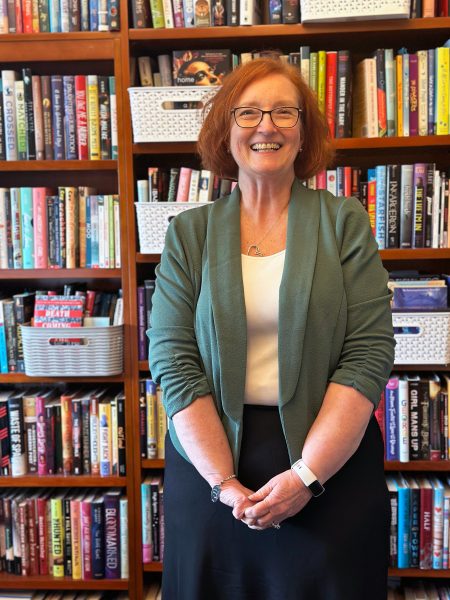 Melanie Hundley stands in front of a bookcase full of books.