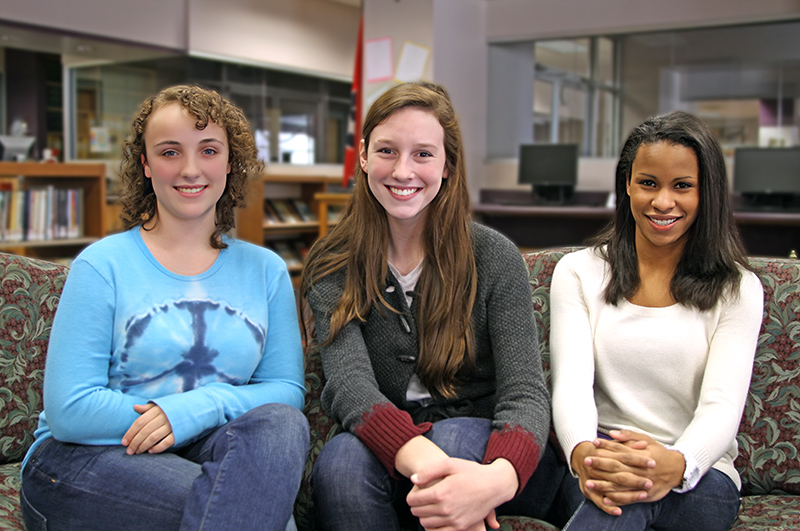 Erin, Hannah, and Kyra smiling and sitting on couch