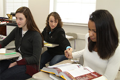 Three students at desks with two of them passing a note