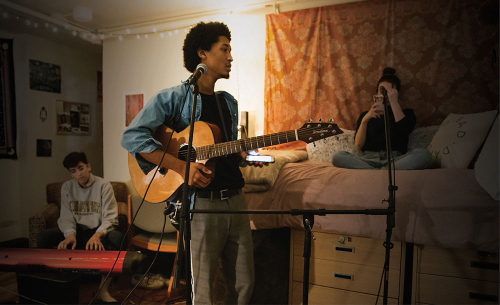 photo of student holding a guitar in a dorm room