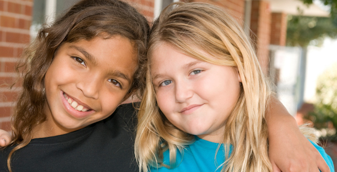 smiling thin brown-skinned girl hugging smiling caucasian overweight girl