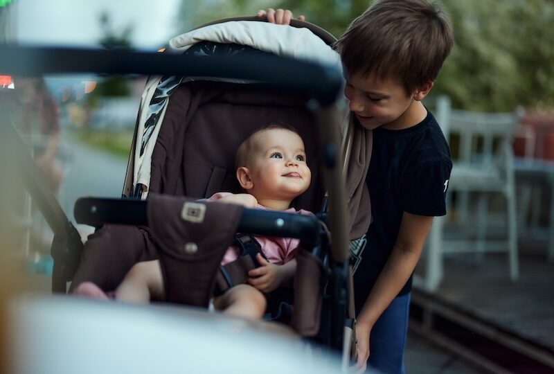 Happy boy enjoying with his baby sister in a stroller during springtime on the street.