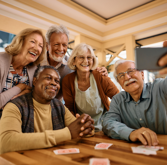 Multiracial group of happy senior people taking selfie with cell phone in nursing home.