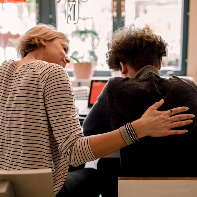 Medium-distance view from the back of a mother sitting at the kitchen table with her teenage boy.