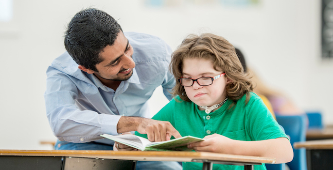 teacher assisting frustrated disabled child with reading