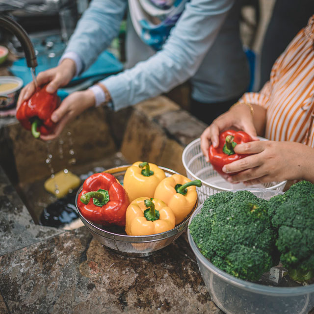 Closeup of two women's hands, washing peppers and broccoli in a sink.