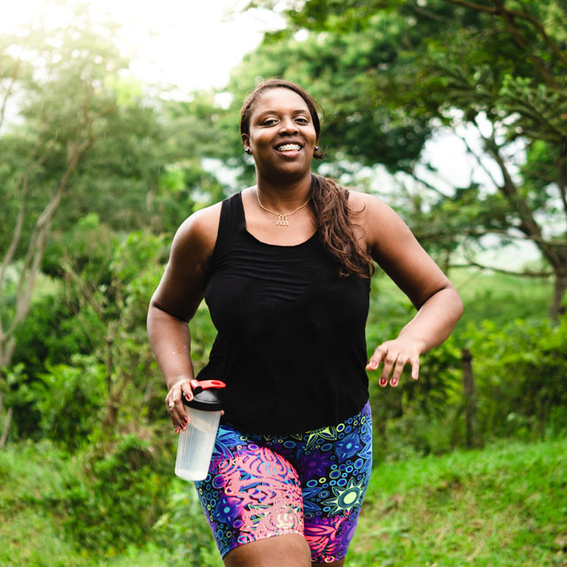 Woman jogging outdoors carrying a water bottle.