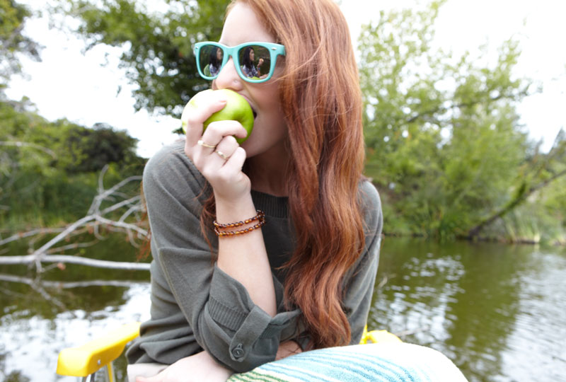 Young woman eats a green apple while sitting outdoors.