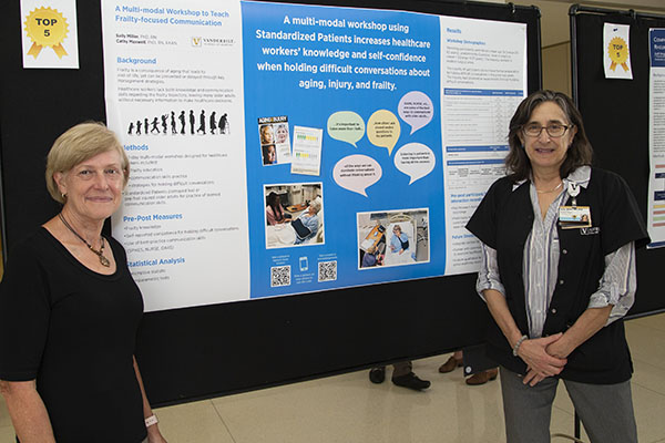 Faculty members Cathy Maxwell and Sally Miller stand on either side of a large poster headlined 