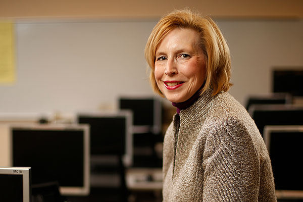 Cathy Ivory sits in a classroom with rows of computer monitors behind her. She's dressed in a suit.