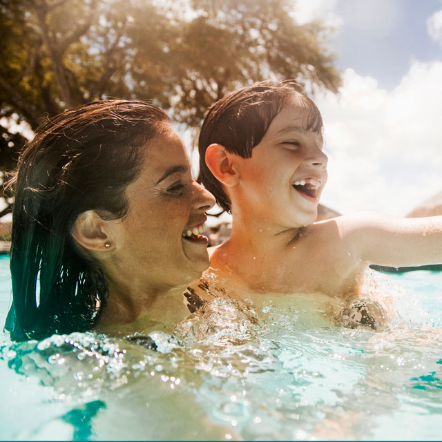 Mother and young son splashing in pool.