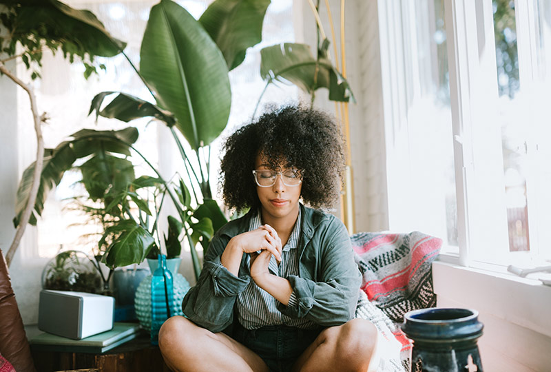 Woman sits on a colorful couch with her eyes closed.