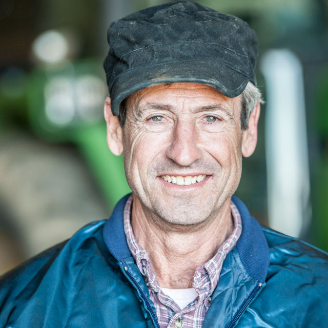 Closeup, head-on portrait of an older man wearing a casual jacket and cap.