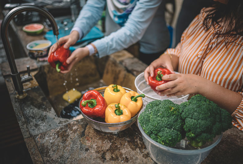 Closeup of two women's hands, washing peppers and broccoli in a sink.