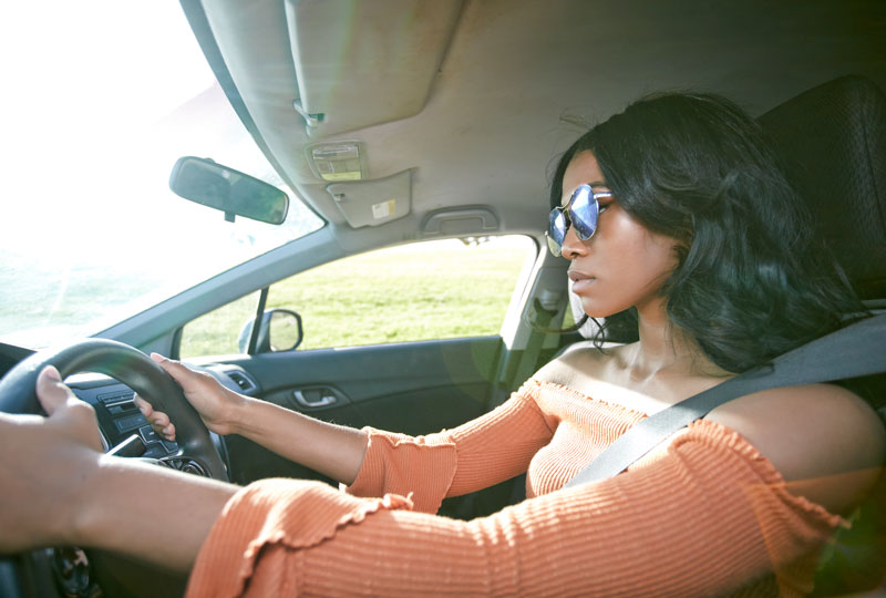 Young woman drives a car along a grassy field