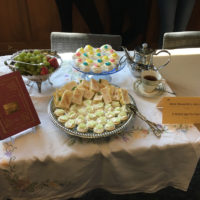 Finger cakes, petite fours, and a tea set laid out on the table.