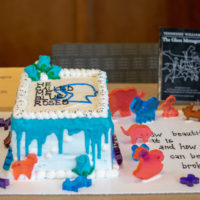 A white cake with blue icing and the quote "He called me blue roses" written in icing.