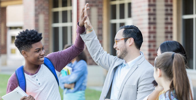 african american teenage high-fives caucasian or hispanic principal outside a school building