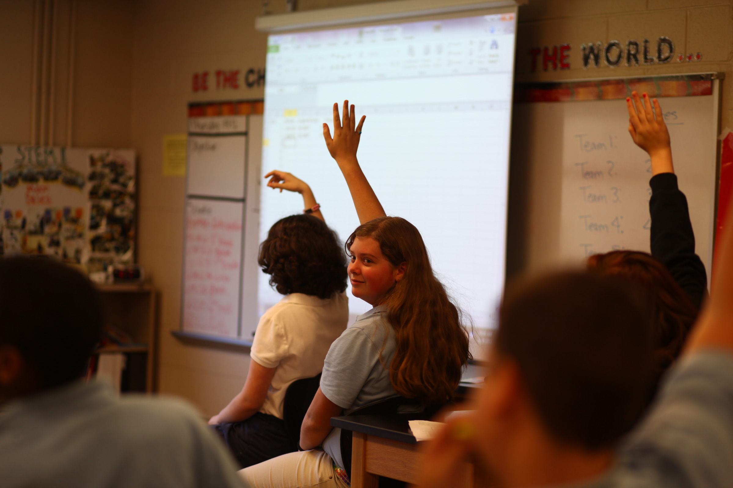 middle school students raising hand in class