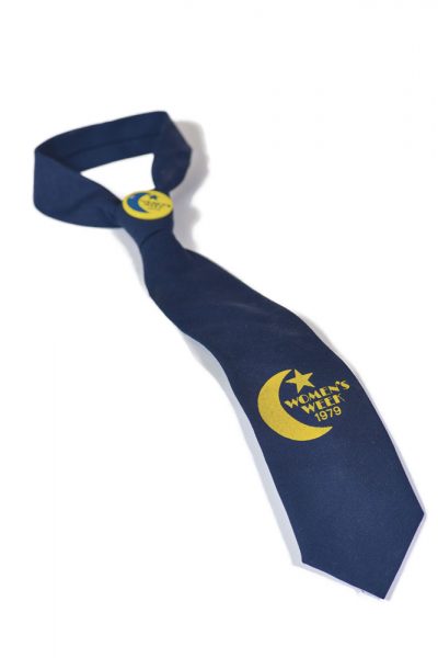 A blue tie and yellow button, both for Women's Week 1979. Now in University Archives