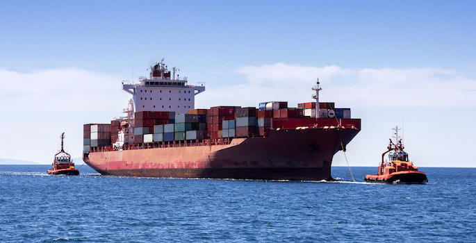 Tugboats pulling container cargo ship to harbor