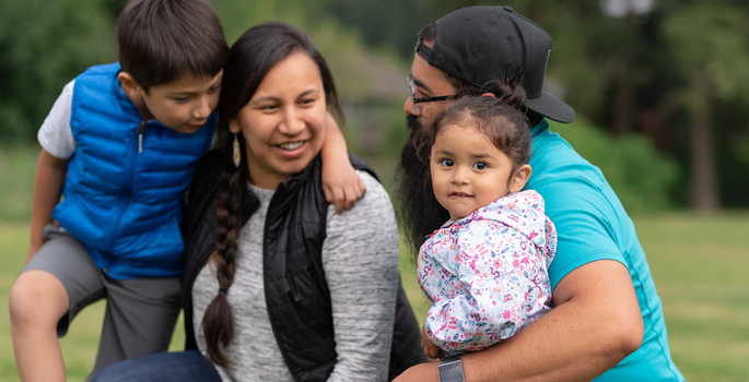Native American family - mom, dad, a eight-year-old boy and a toddler girl wearing casual fall clothing playing on a soccer a field on an autumn day