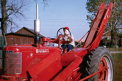 A young child sits in a much-larger-than him red tractor. The child is wearing a matching red cap.