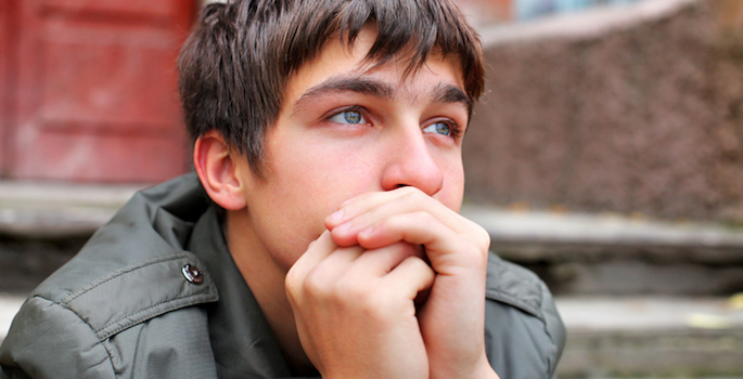 sad or anxious young white man sitting on front porch of apartment building with his hands clasped