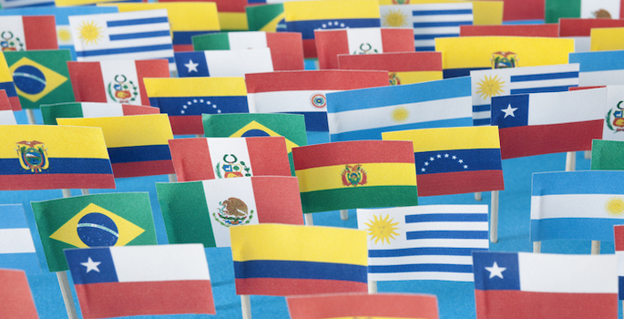 Lots of small handmade flags of latin american countries over blue background