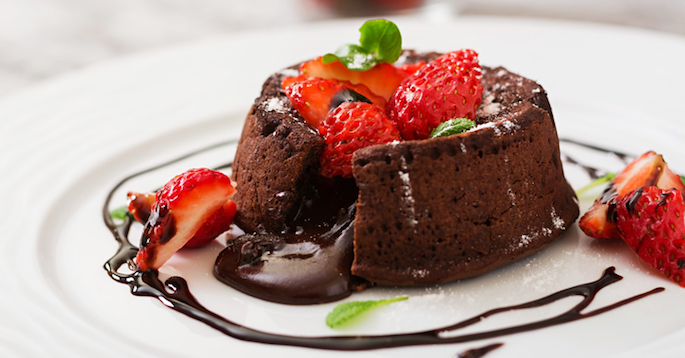 Fancy molten chocolate cake with raspberries and chocolate swirls on white plate